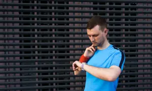 Mężczyzna w sportowej koszulce sprawdza na zegarku tętno spoczynkowe u sportowców.