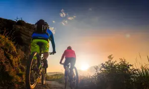 Dwie osoby na rowerach górskich przemierzają malownicze **trasy velo Polska** o zachodzie słońca.