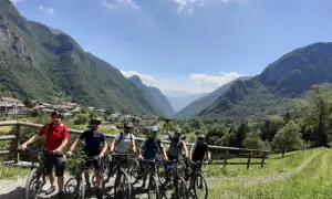 Grupa rowerzystów na malowniczym szlaku stu jezior, podziwiająca górską panoramę i urokliwą wioskę.