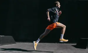 Mężczyzna w pomarańczowych spodenkach i żółtych butach biegnie dynamicznie. To inspiracja, jak przebiec 10 km.