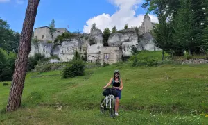 Kobieta z rowerem na tle ruin zamku na Szlaku Orlich Gniazd.