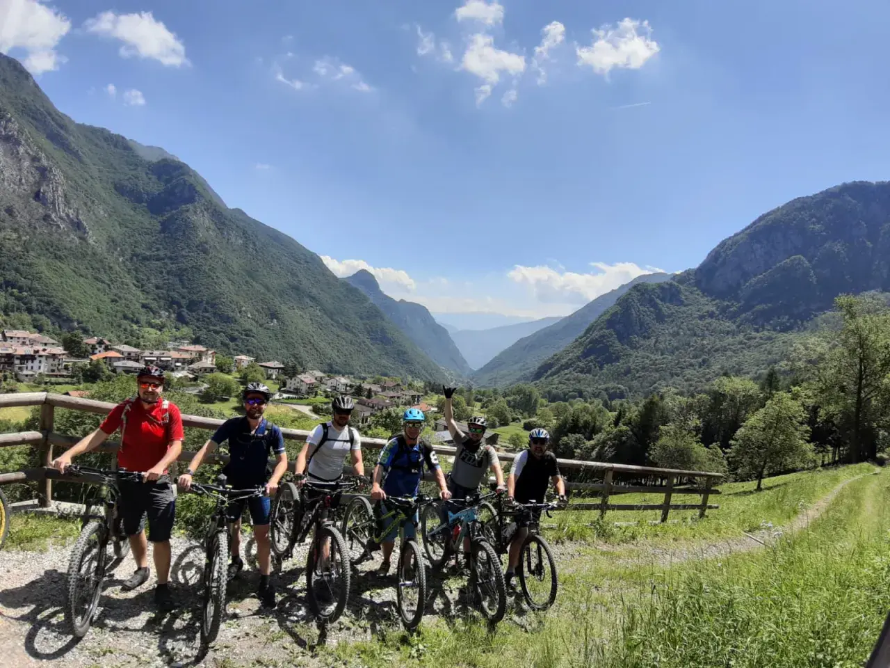 Grupa rowerzystów na malowniczym szlaku stu jezior, podziwiająca górską panoramę i urokliwą wioskę.