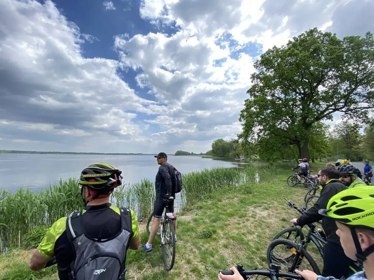 Grupa rowerzystów odpoczywa nad jeziorem, podziwiając malownicze stawy milickie trasy rowerowe.