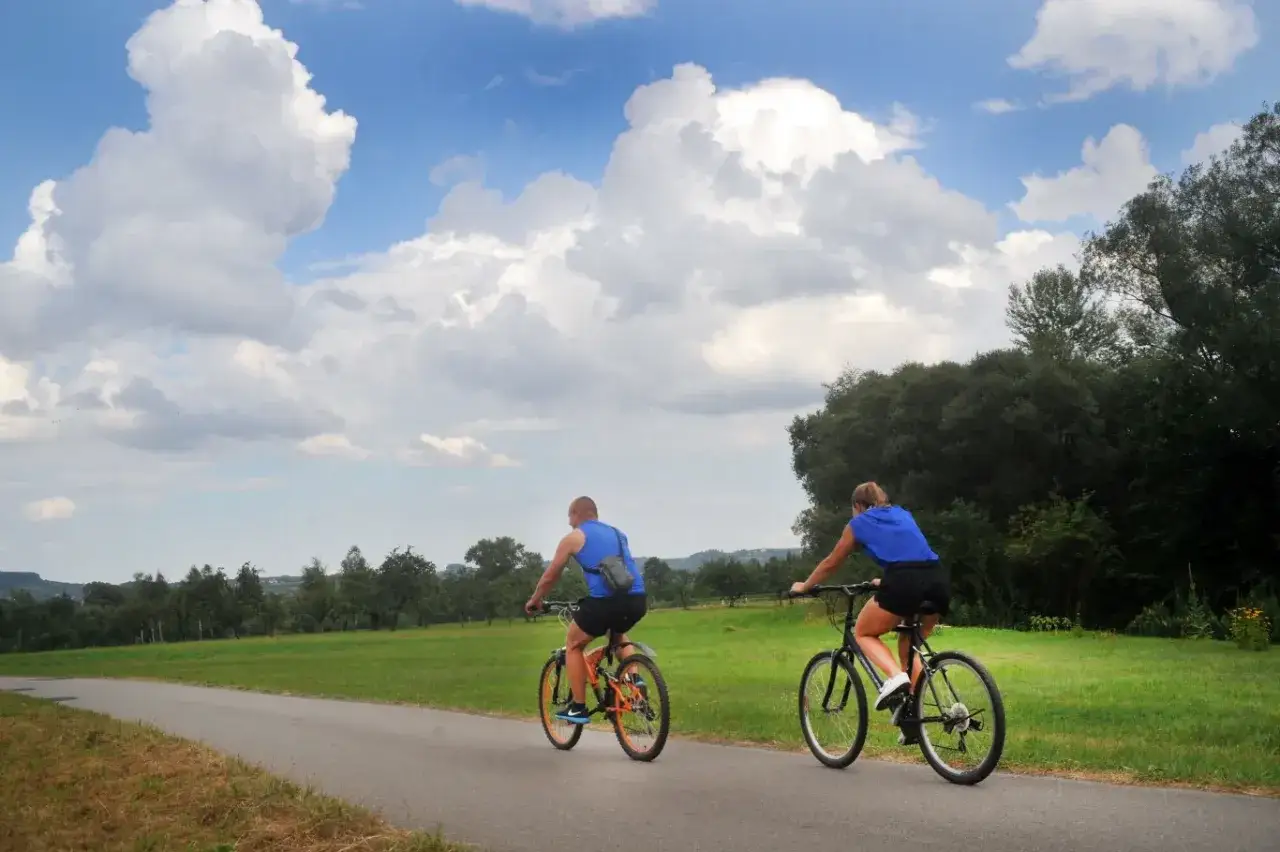 Para rowerzystów przemierza malownicze trasy rowerowe łódzkie. Piękne chmury na niebie dodają uroku krajobrazowi.