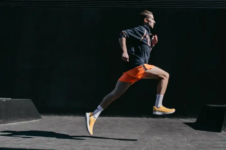 Mężczyzna w pomarańczowych spodenkach i żółtych butach biegnie dynamicznie. To inspiracja, jak przebiec 10 km.